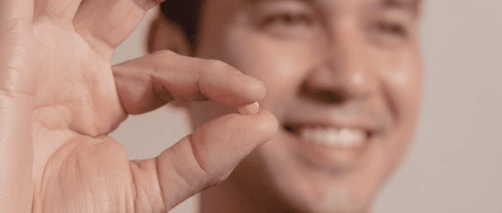 Close-up of a smiling man holding a single small hair treatment chew between his thumb and index finger.